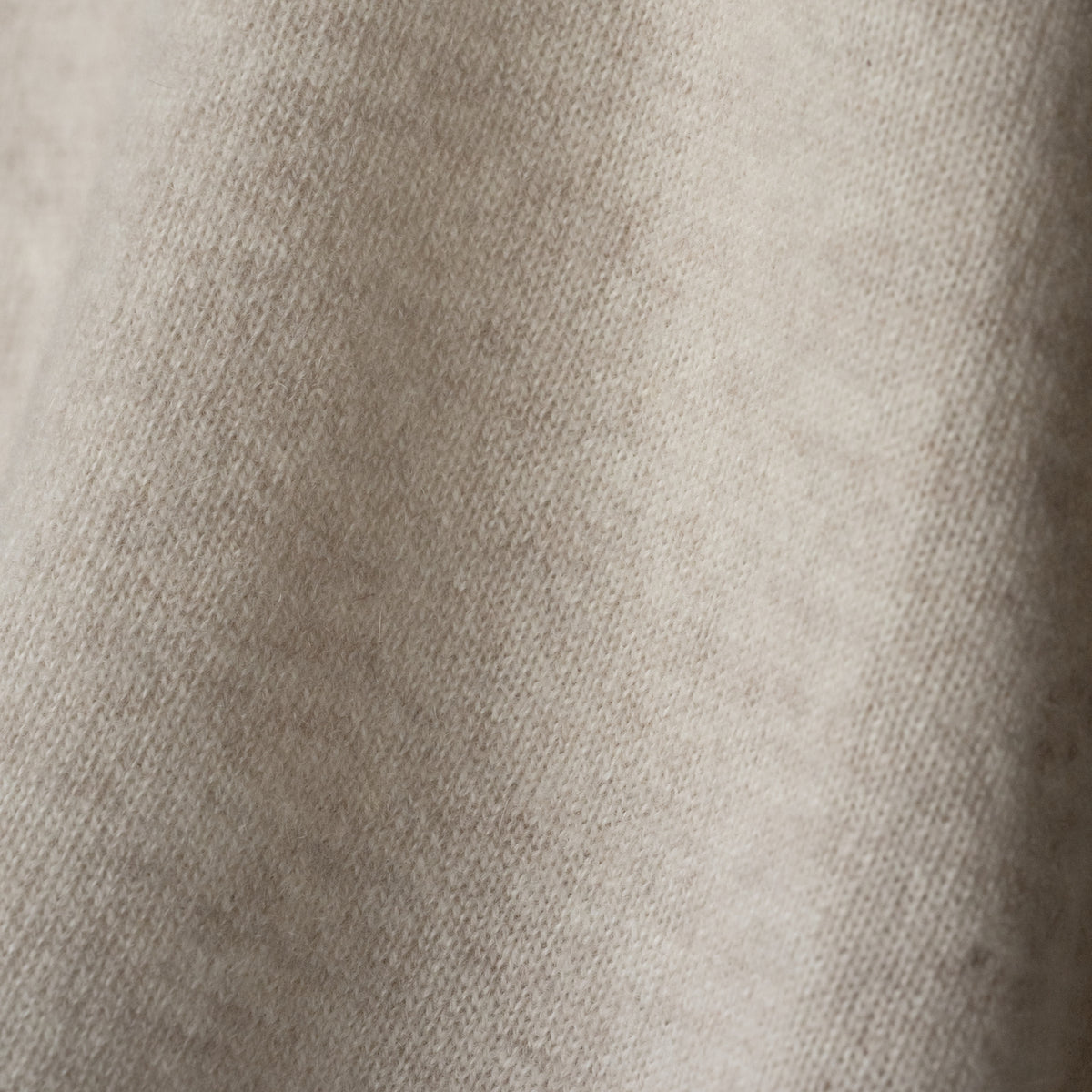 Close-up of Ninepine's 100% cashmere sweater fabric, showcasing its soft, fine knit texture in a neutral beige shade.