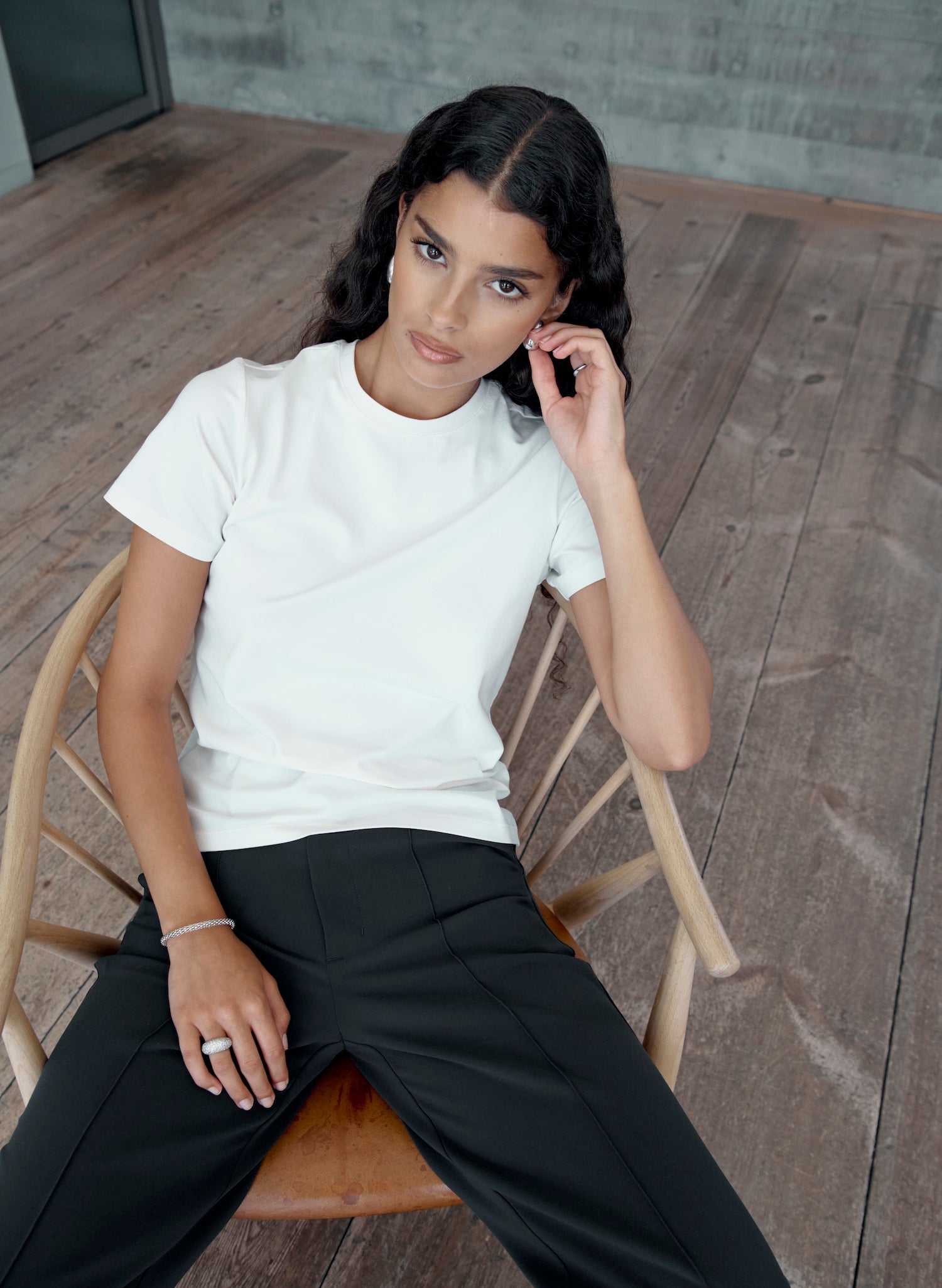 Woman seated wearing a white fitted Pima cotton t-shirt with high-waisted black trousers, showcasing a clean, minimal outfit with a flattering tailored fit